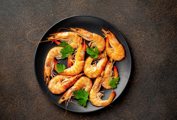 raw prawns waiting for the cook to grill, in a black plate with herbs and spices on a stone background 