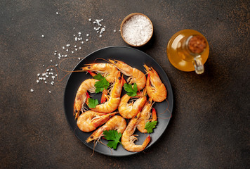 raw prawns waiting for the cook to grill, in a black plate with herbs and spices on a stone background 