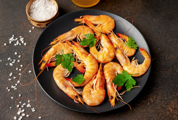 raw prawns waiting for the cook to grill, in a black plate with herbs and spices on a stone background 