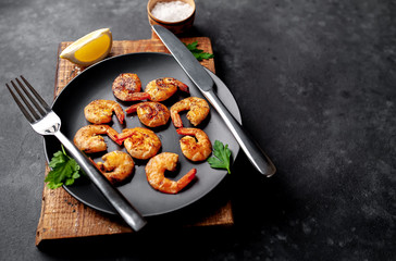 grilled shrimps, with lemons, herbs and spices, served on a black plate on a stone background with copy space for your text