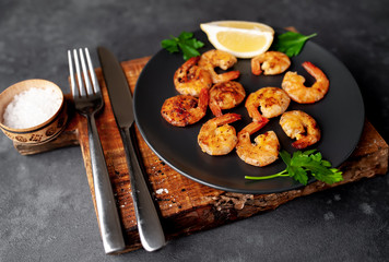 grilled shrimps, with lemons, herbs and spices, served on a black plate on a stone background 