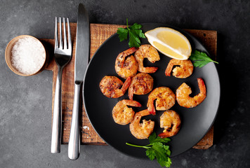 grilled shrimps, with lemons, herbs and spices, served on a black plate on a stone background 