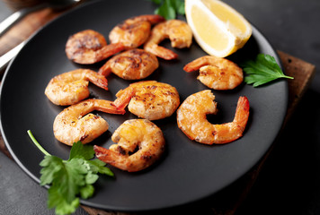 grilled shrimps, with lemons, herbs and spices, served on a black plate on a stone background 