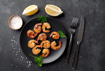 Fototapeta na wymiar grilled shrimps, with lemons, herbs and spices, served on a black plate on a stone background 