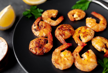 grilled shrimps, with lemons, herbs and spices, served on a black plate on a stone background 
