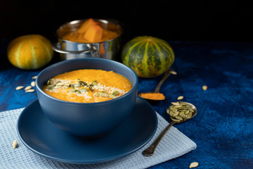 pumpkin cream soup in a blue plate on a deep classic blue background with slices of pumpkin with blue textile and a spoon.