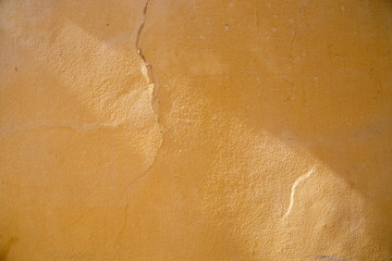 Fototapeta premium Cracks in the paint on wavy and uneven surface of a yellow bumpy wall.