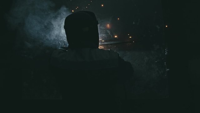 Forge workshop. Smithy. Worker in a welding hood helmet welds a part by electric welding. Sparks are reflected in the protective screen. Blacksmith makes iron product for manufacture. Slow motion.
