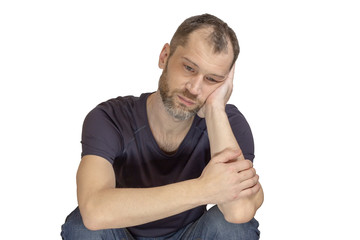 A sad young unshaven man in a black t-shirt and blue jeans sits with his cheek propped on his hand, his depression a Selective focus. isolated.