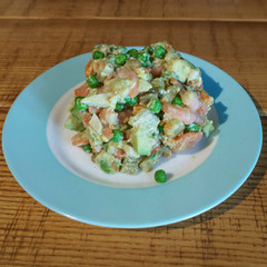 Olivier salad in a blue plate stands on a wooden table.