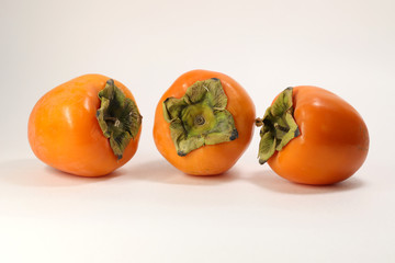 Three ripe bright orange beautiful pieces of persimmon Oriental. Selective focus. On white background