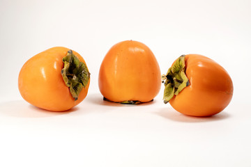 Three ripe bright orange beautiful pieces of persimmon Oriental. Selective focus. On white background