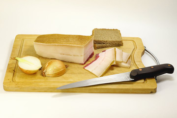 Slices of bacon cut with a knife from a whole piece on a wooden Board, next to a chopped onion and rustic bread made of rye flour. Selective focus. On white background