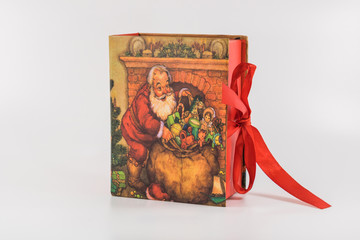 Cadeau de noël boite fermée par un ruban rouge avec un décor traditionnel de noël et un dessin de père noël distribuant les cadeaux photo studio sur fond blanc