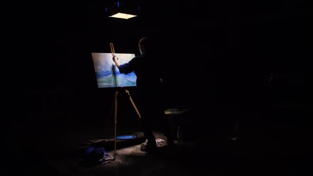Artist copyist paint seascape with ship in ocean. Craftsman decorator draw as boat sail on blue sea with acrylic oil color. Black background. Indoor. Wide angle shot cinematic look.