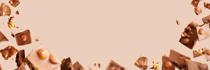 Flying in the air broken bar of milk chocolate with nuts and flakes on pastel pink background....
