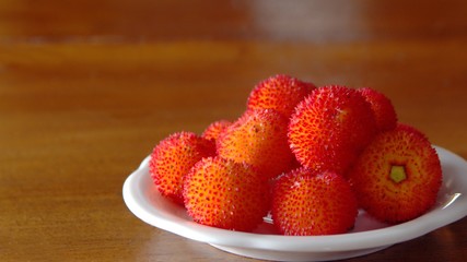 Irish strawberries (Arbutus unedo) served on a dish on a wooden table.