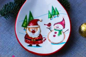 Christmas decorations. Decorative white tableware with the image of Santa Claus, snowman and Christmas trees. Chocolates in festive packaging. Ribbon for decoration. Christmas background.