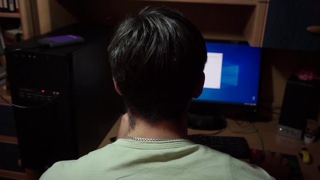 Close-up, nape young guy s head, computer case, looks monitor, closes windows, tabs, programs with mouse, sits table. Night, dark, evening, apartment, room house static camera
