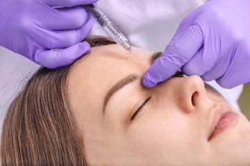 Beautician makes injections between the eyebrows on the face of a beautiful woman. Correction of mimic wrinkles. Cosmetology Cosmetic procedures in the medical center. Closeup.