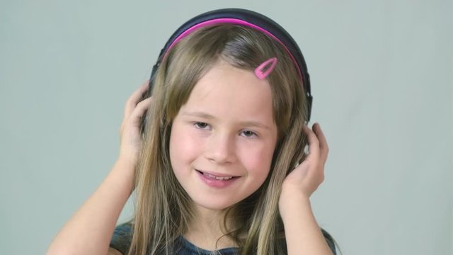 Pretty smiling cild girl listening to music in big pink earphones.