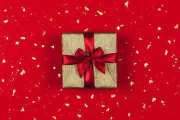 Golden gift box with red bow on the red background with golden sparkles.