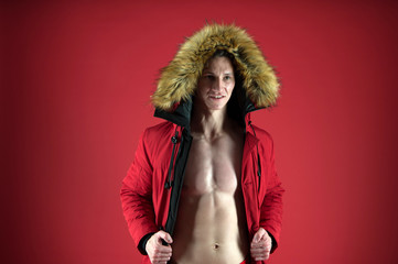 muscular guy wear warm clothes. christmas time. xmas winter holiday activity. its cold outside. male winter fashion. macho man in warm puffer jacket. sexy man with fit body red background