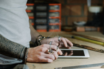 Craftsman artist using a tablet and checking some ideas for a new designer wooden product in his home workshop while smoking a cigarette