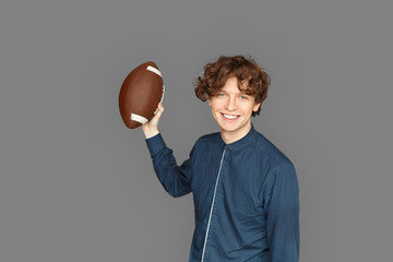 Sporty Lifestyle. Teenager boy standing isolated on grey playing with american football ball laughing cheerful