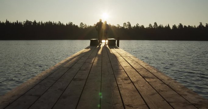 Man and woman walking on wooden boardwalk and jetty on lake in morning