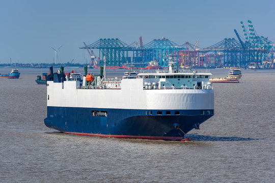 Large White and blue Roll-on roll-off or ro-ro ship or vehicle carrier vessel anchored in front of piers.