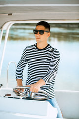 A young and handsome Caucasian man in glasses sailing in the sea on a boat on a sunny day.