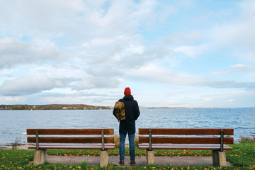 Man with backpack enjoy panorama by the Bodensee lake. Landscape in Switzerland. Happy man in travel. Amazing scenic outdoors view. Dramatic sky. Swans on water. Adventure lifestyle, freedom