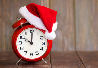 Christmas time concept, red santa hat alarm clock on a brown wooden background