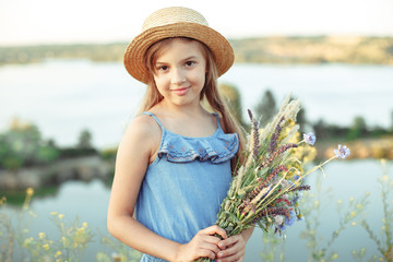 Little girl in a straw hat with a bouquet of wildflowers on a background of a beautiful landscape