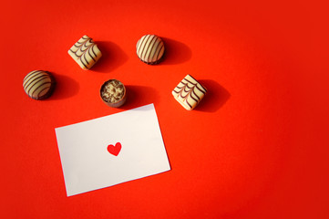 St. Valentine's Day. Chocolate candies and a note with a heart on red background. Chocolate candies. Chocolate treats. Assorted chocolates.