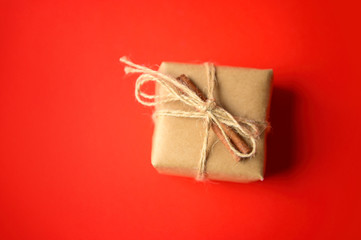 A small gift box in craft paper is decorated with cinnamon on a red background. Little present. A small gift in plain paper.