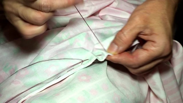 an adult woman seamstress sews impales the fabric with a needle. Hands close up. grandma makes a smooth hand stitch. Making clothes and sewing colored bed linen at home or in a garment factory