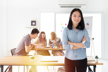 Fototapeta premium attractive asian businesswoman standing and cross arm in office, blurred officer team discuss and sharing information, they planing project together, organization management