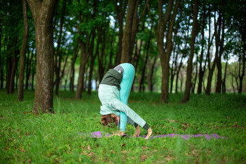 A young sports girl practices yoga in a quit green summer forest, yoga assans posture. Meditation and unity with nature