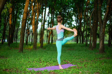Fototapeta premium A young sports girl practices yoga in a quit green summer forest, yoga assans posture. Meditation and unity with nature