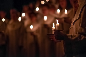 People are handling candles in the traditionall religious habit dresses in the church. Celebration of Lucia day, Sweden - obrazy, fototapety, plakaty