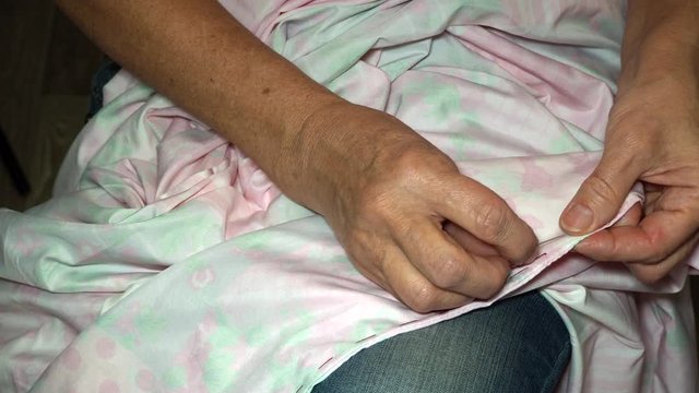 an adult woman seamstress sews impales the fabric with a needle. Hands close up. grandma makes a smooth hand stitch. Making clothes and sewing colored bed linen at home or in a garment factory
