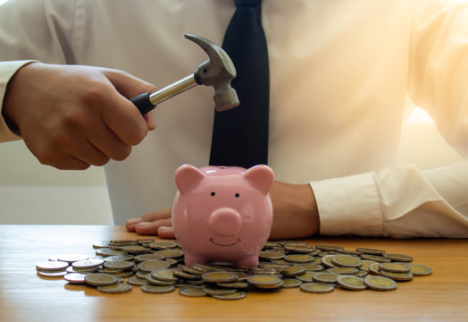 A business man with a hammer ready to smash a piggy bank on a wooden table - Powered by Adobe