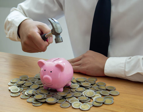 A business man with a hammer ready to smash a piggy bank on a wooden table