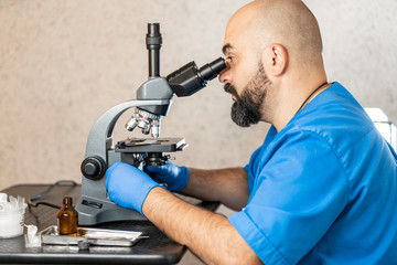 Male laboratory assistant examining biomaterial samples in a microscope