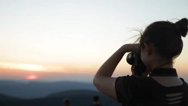 The silhouette of a young woman taking a photo of the sunset.