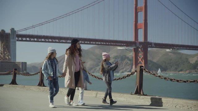 Girl walking near Golden Gate Bridge with family and photographing scenic view / San Francisco, California, United States