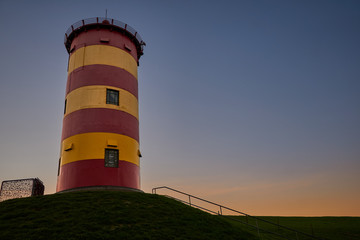 Pilsum, Lower Saxony/ Germany: Red and yellow lighthouse during sunset and blue sky