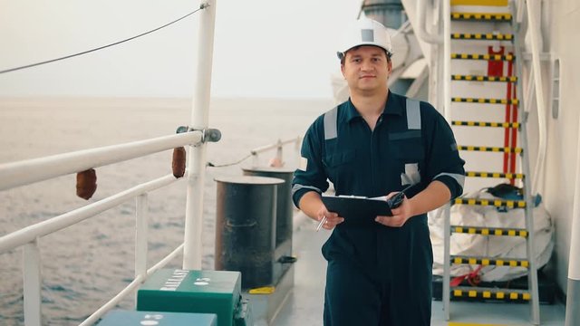 Marine chief officer or chief mate on deck of ship or vessel. He fills up ahts vessel checklist. Ship routine paperwork. He holds VHF walkie-talkie radio in hands.